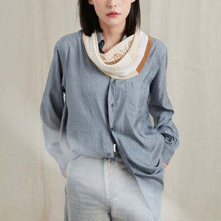 Beige and sage green monogram silk scarf elegantly draped around neck, paired with light blue button-up shirt and light denim