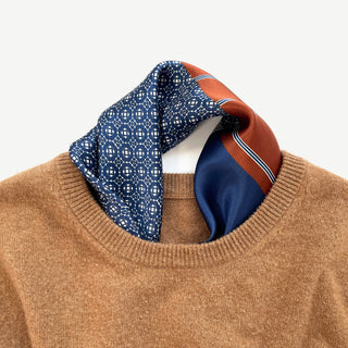 Navy silk square with geometric pattern and rust-colored border elegantly styled with camel sweater, showing luxurious sheen and drape
