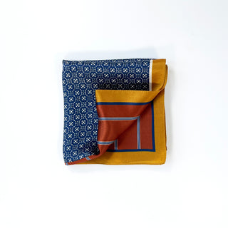 Navy silk neckerchief with white geometric pattern, folded to display rust orange and gold borders, showcasing luxurious fabric sheen
