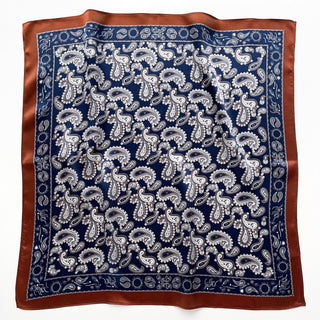 Navy blue silk scarf with white paisley pattern and rustic brown border, displayed flat to show detailed design