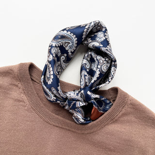 Navy blue silk scarf with white paisley pattern tied as a neckerchief around the collar of a light brown sweater