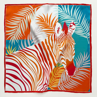 Luxury silk scarf featuring vibrant orange and teal zebra print with tropical palm leaves, bordered by hand-rolled red edges on premium twill fabric.