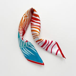 Double-sided silk bandana featuring vibrant orange and red zebra print pattern with contrasting turquoise botanical design, elegantly displayed against white background