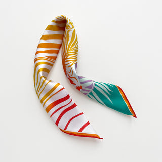 Double-sided silk scarf with vibrant zebra print pattern in gold, red, and teal colors, elegantly draped to show both sides on white background