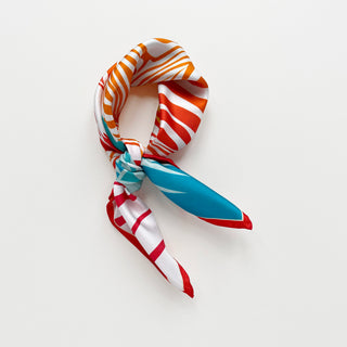 Double-sided silk bandana featuring vibrant orange, red and turquoise zebra print pattern, tied in an elegant knot against white background
