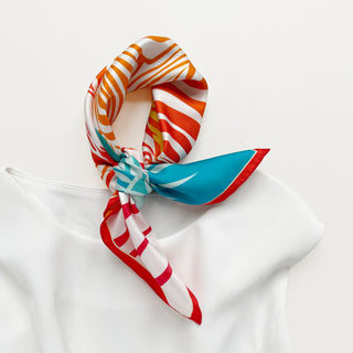 Double-sided silk bandana tied in a knot showcasing vibrant orange, red, and turquoise zebra print patterns with elegant hand-rolled edges on white background