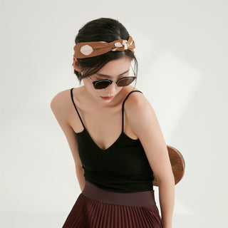 Silk scarf styled as headband in ochre with polka dots, worn with black tank top and burgundy pleated skirt, demonstrating versatile styling