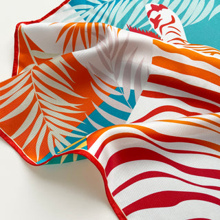Luxurious double-sided silk scarf featuring vibrant tropical palm patterns in orange, teal, and white with red trim and hand-rolled edges