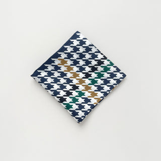 Luxury silk scarf with navy houndstooth pattern accented with green and gold, folded into a square showing hand-rolled edges