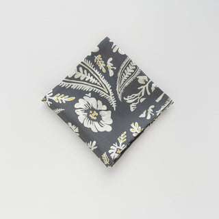 Folded ash grey silk scarf with elegant white botanical pattern featuring flowers, leaves, and subtle yellow accents, displayed on white background