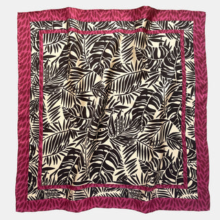 Luxury silk scarf featuring black tropical leaf pattern on light beige background with decorative magenta leaf border, displayed flat showing hand-rolled edges