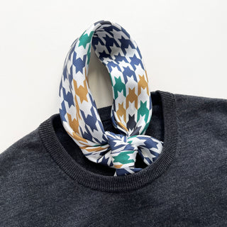 Luxury silk scarf with navy, green, and gold houndstooth pattern elegantly tied around a dark gray sweater neckline, showcasing its sophisticated design.