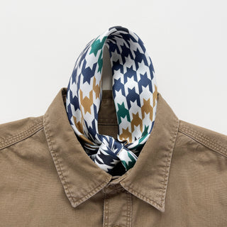Luxurious silk scarf with navy, green, and gold houndstooth pattern styled elegantly around collar of tan shirt, showcasing hand-rolled edges