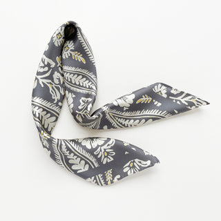 Ash grey silk scarf with elegant white botanical print and yellow accents, featuring hand-rolled edges and flowing twill fabric texture