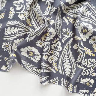 Ash grey silk scarf with elegant white floral and leaf pattern featuring delicate yellow accents, displaying luxurious fabric texture and hand-rolled edge