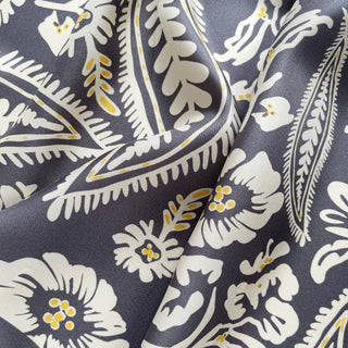 Close-up of ash grey silk scarf featuring elegant white floral pattern with yellow accents, showing the luxurious twill texture and fabric drape