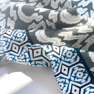 Teal green silk scarf with contrasting geometric patterns - diamond shapes in blue and white alongside gray zigzag design, showing luxurious hand-rolled edges
