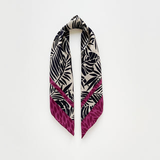 Luxury silk scarf featuring black tropical foliage pattern on ivory background with magenta leaf-print border, displayed in elegant drape