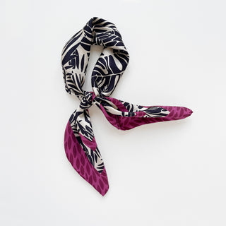 Silk scarf featuring black tropical foliage pattern on ivory background with magenta leaf-patterned border, elegantly tied in a loose knot
