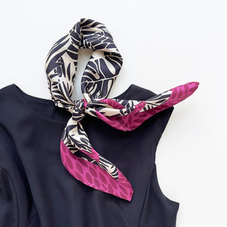 Luxury silk scarf with black tropical foliage pattern on ivory background, magenta leaf border, styled in a knot on black garment