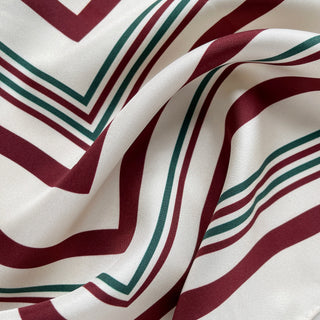 Luxurious silk twill scarf with geometric pattern featuring burgundy and green stripes on cream white background, showing smooth fabric texture