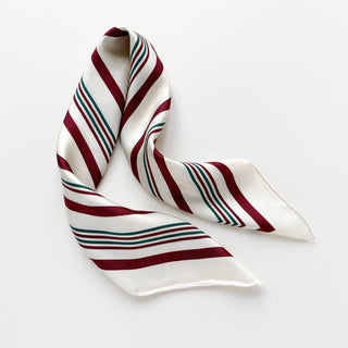 Luxurious silk scarf with modern striped pattern in burgundy and green on cream white background, featuring hand-rolled edges and smooth twill texture.