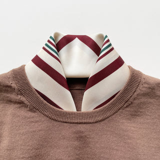 Luxury silk scarf with cream base and burgundy/green geometric pattern stylishly worn with brown sweater, showcasing double-sided design and hand-rolled edges