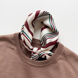 Luxurious silk scarf with burgundy and green stripes on cream background, elegantly tied around neck of dusty rose sweater