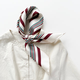 Burgundy Mod Quad silk scarf tied elegantly at neck of white shirt, featuring diagonal burgundy and green stripes on cream background