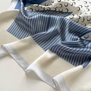 Lunar Peaks silk scarf featuring French blue herringbone pattern with cream border and black crescent moon design, elegantly draped to show luxurious texture