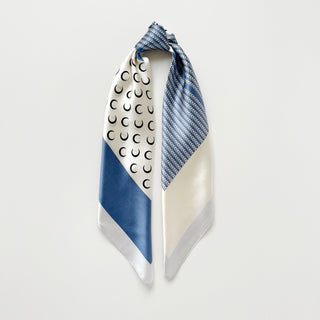 Silk scarf with geometric design featuring French blue sections with chevron pattern and white panels with crescent moon motifs, elegantly folded