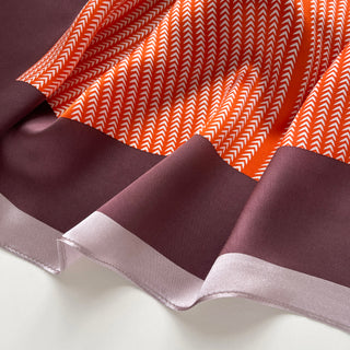 Luxurious silk scarf featuring tangerine orange with white herringbone pattern and deep blue-purple border with light lilac trim, elegantly draped