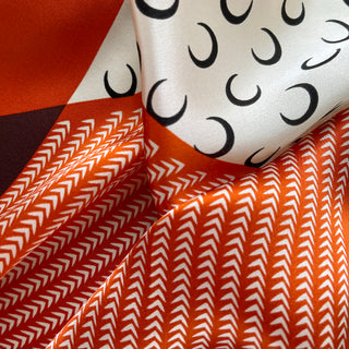Silk scarf featuring tangerine chevron pattern and cream fabric with black crescent moons, showing luxurious fabric texture and drape