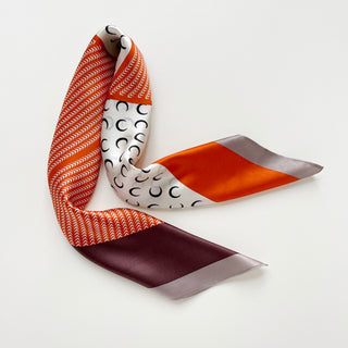 Lunar Peaks silk scarf featuring tangerine chevron pattern, white with crescent moon motifs, and French blue color blocks, elegantly draped on white background.
