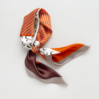 Tangerine & French Blue Lunar Peaks silk scarf with zigzag pattern, crescent moon design, and color blocks of white, orange and blue, elegantly knotted