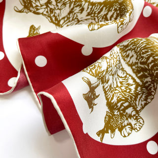 Luxurious silk scarf featuring red polka dots and gold paw print design with hand-rolled edges, showcasing rich texture and elegant sheen