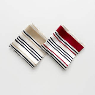 Two folded silk scarves with striped patterns - one with beige and navy stripes, and one with red and navy stripes on off-white background