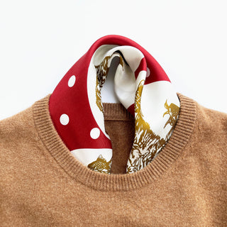 Red and white silk bandana with polka dots and gold paw prints elegantly styled around the neckline of a camel-colored sweater.