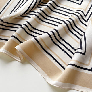 Luxurious silk scarf with geometric pattern featuring navy and beige stripes on off-white background, displaying soft texture and elegant drape