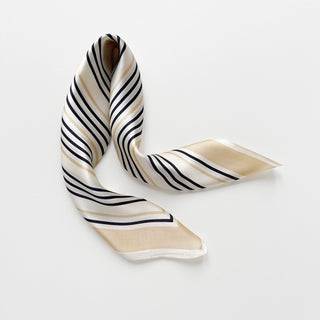 Luxurious silk bandana scarf with diagonal navy and beige stripes on creamy white background, elegantly draped to showcase shimmering texture