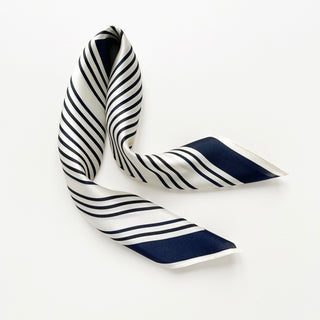 Elegant silk scarf with navy and white diagonal stripes pattern displayed on white background, showing luxurious sheen and smooth texture