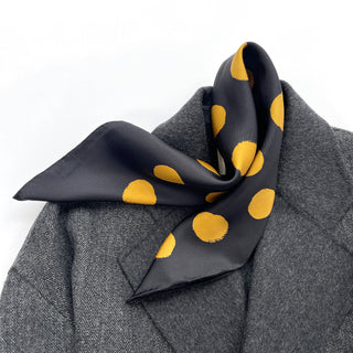 Black silk bandana scarf with ochre polka dots elegantly styled on grey coat collar, showcasing the luxurious texture and hand-rolled edges