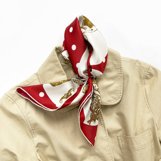 Red silk bandana scarf with white polka dots and gold paw prints, styled as a neckerchief on a beige shirt collar.
