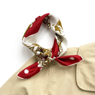 Silk bandana scarf with red polka dot pattern and gold paw prints on cream background, styled in a knot on a beige garment collar