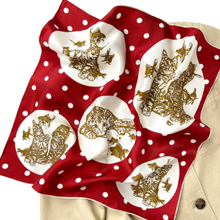 Red silk scarf with white polka dots featuring gold cat and fish illustrations in white medallions, displayed with hand-rolled edges