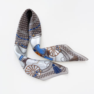 Luxury silk square scarf with equestrian baroque pattern featuring blue chains, wooden carriage wheels, tassels, and silver accents on a gray geometric background