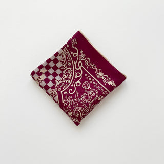 Burgundy silk bandana with ornate baroque pattern and checkerboard design, folded into a square showing hand-rolled edges on white background