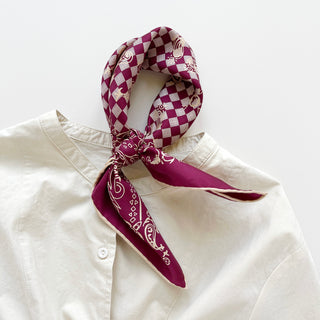 Burgundy silk bandana with checkered pattern and paisley border, elegantly tied around collar of white shirt, showing hand-rolled edges
