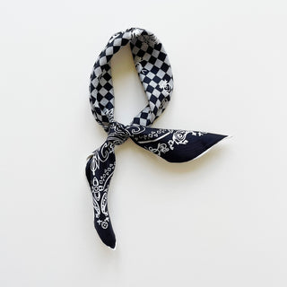Silk bandana with black and white checker pattern and baroque design, elegantly tied against white background showing hand-rolled edges