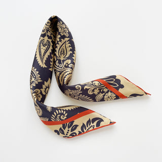 Navy and beige silk scarf displaying intricate paisley pattern with vibrant orange border, elegantly arranged to showcase hand-rolled edges and luxurious sheen